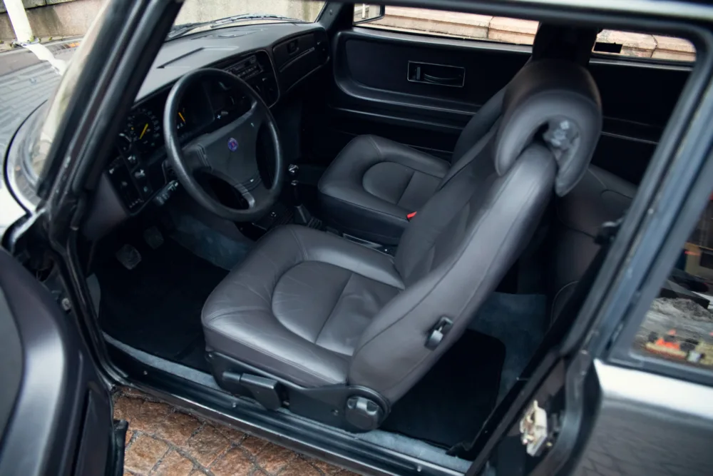Car interior with open door and gray leather seats.