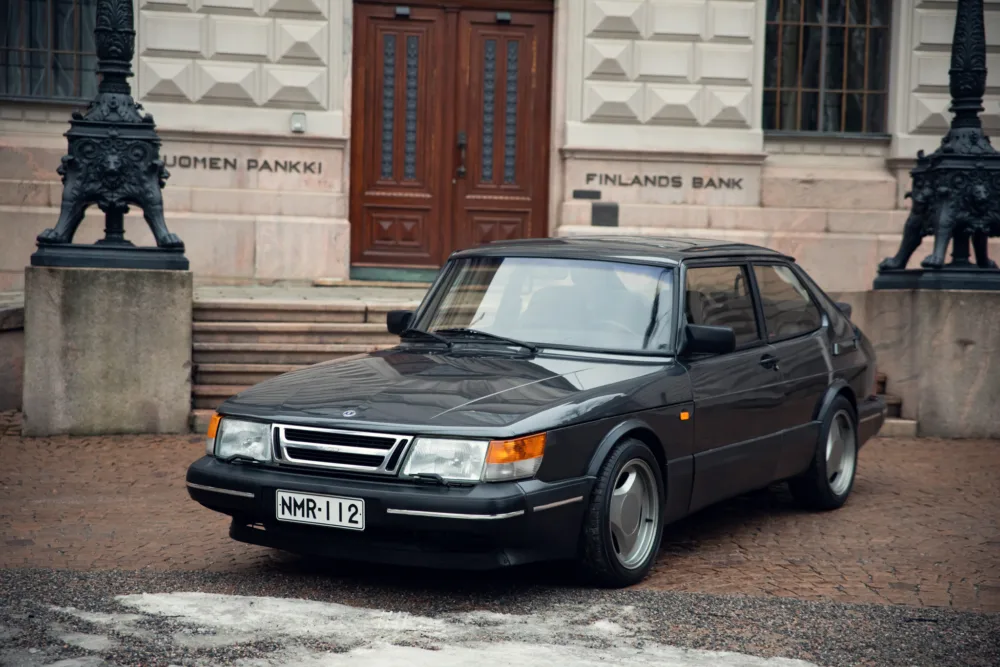 Vintage Saab car parked in front of bank building.