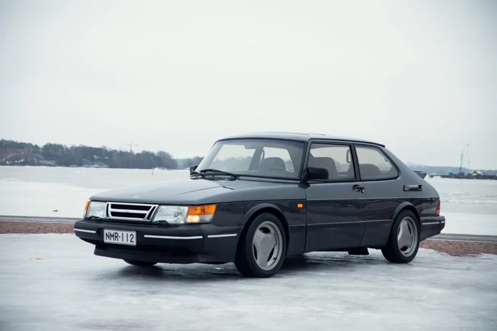 Vintage car on icy road near water.