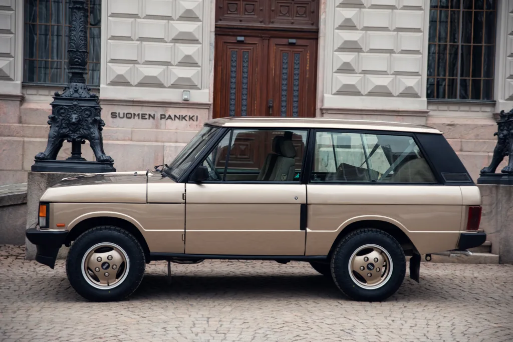 Vintage beige SUV parked by building entrance.