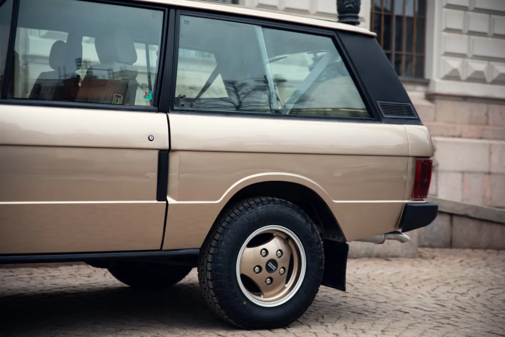 Vintage beige car parked on cobblestone street.