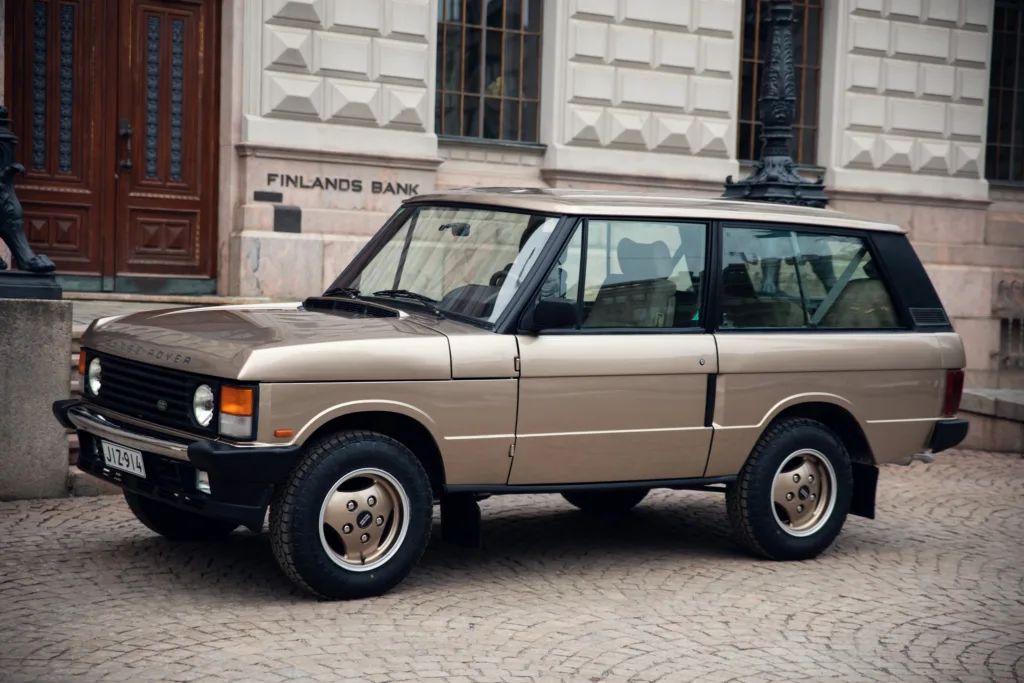 Vintage beige SUV parked on cobblestone street.