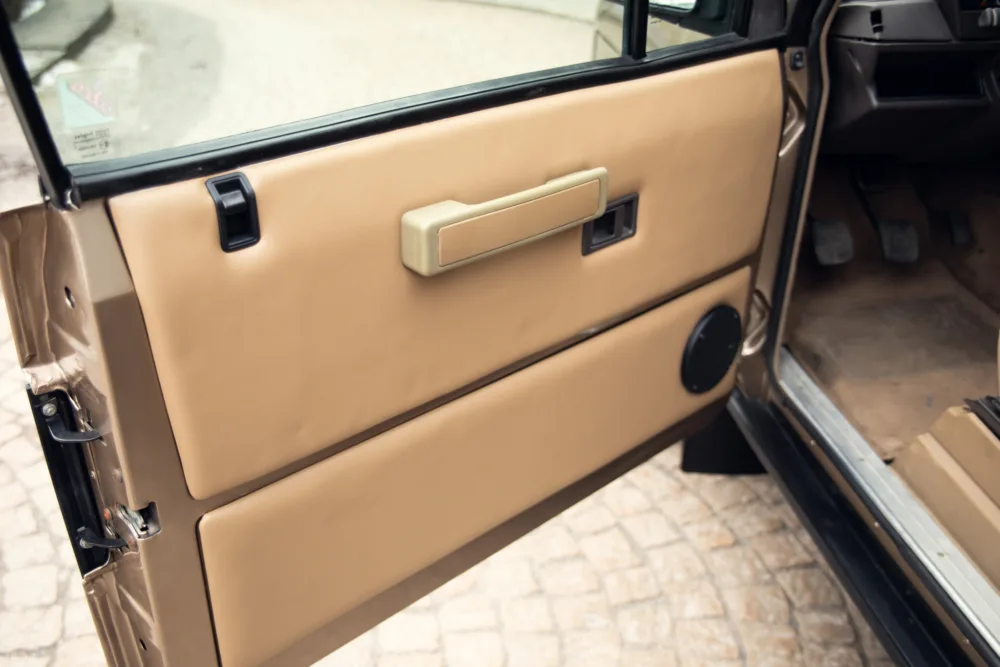 Beige car door interior with handle and controls.