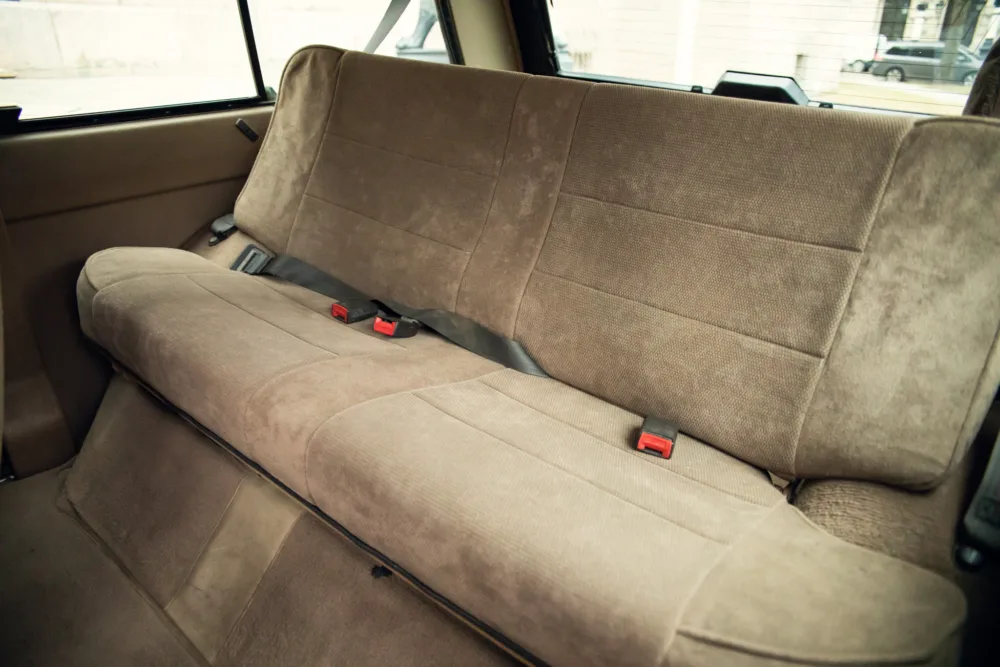 Rear car seat with seatbelts and beige upholstery.