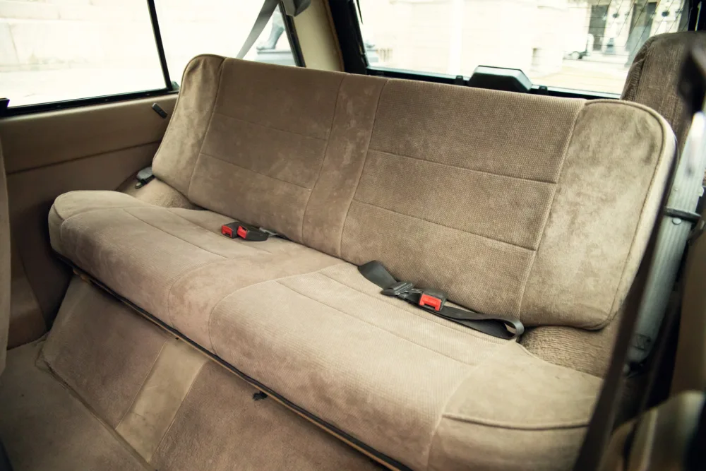 Vintage car's beige rear seat with seatbelts.