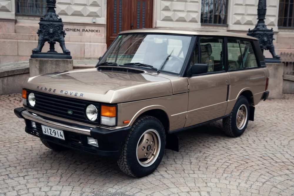 Vintage beige Range Rover parked on cobblestone street.