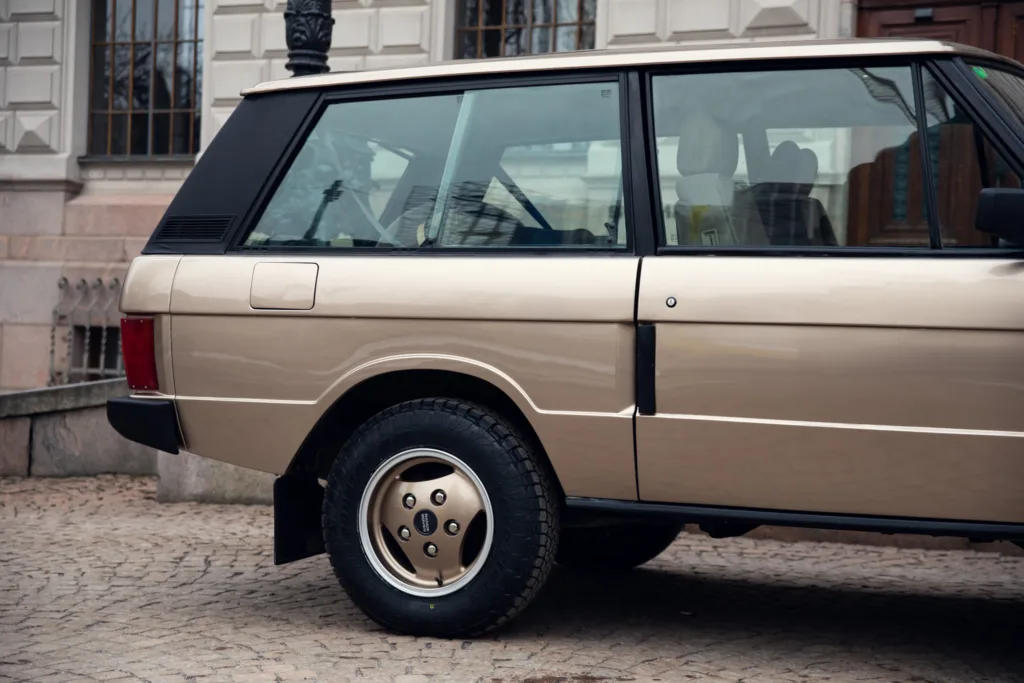 Beige vintage SUV parked on cobblestone street.