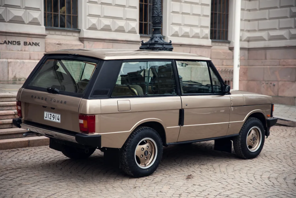 Vintage beige Range Rover parked on cobblestone street.