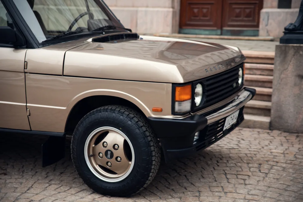 Vintage beige Range Rover parked on cobblestone street.