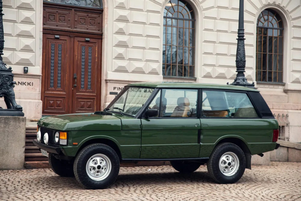 Vintage green SUV parked by historical building.