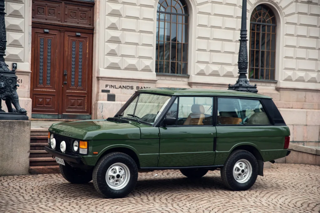 Vintage green SUV parked by historic building.
