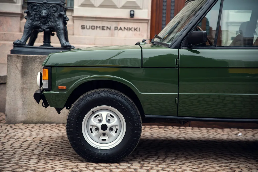 Classic green SUV parked on cobblestone street.