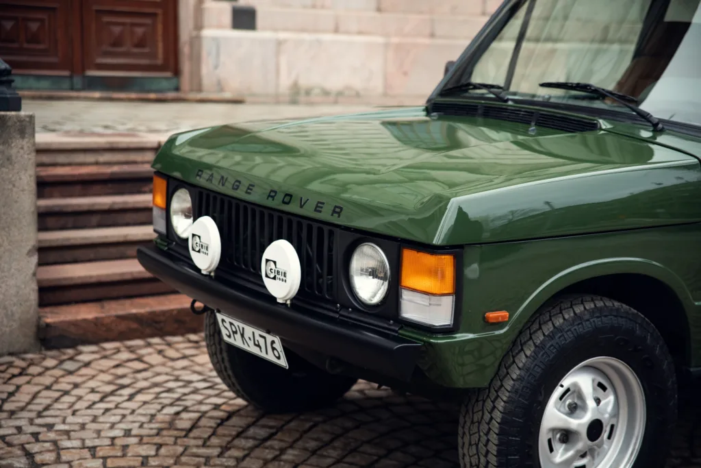 Green Range Rover classic parked on cobblestones.