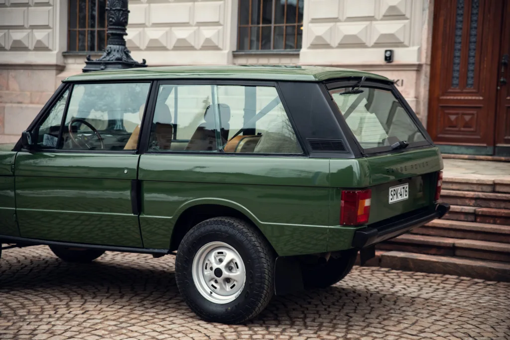 Green vintage Range Rover parked on cobblestone street.