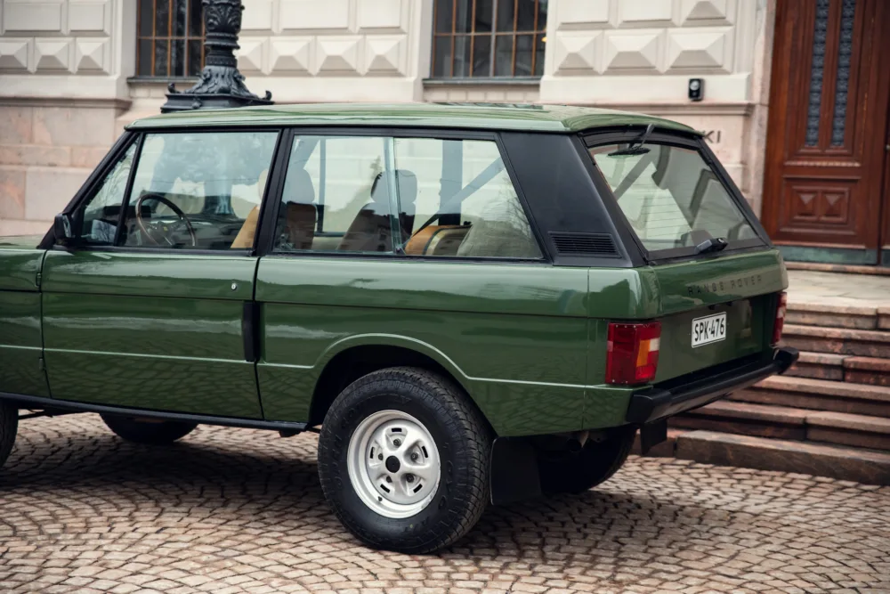 Vintage green Range Rover parked on cobblestone street.