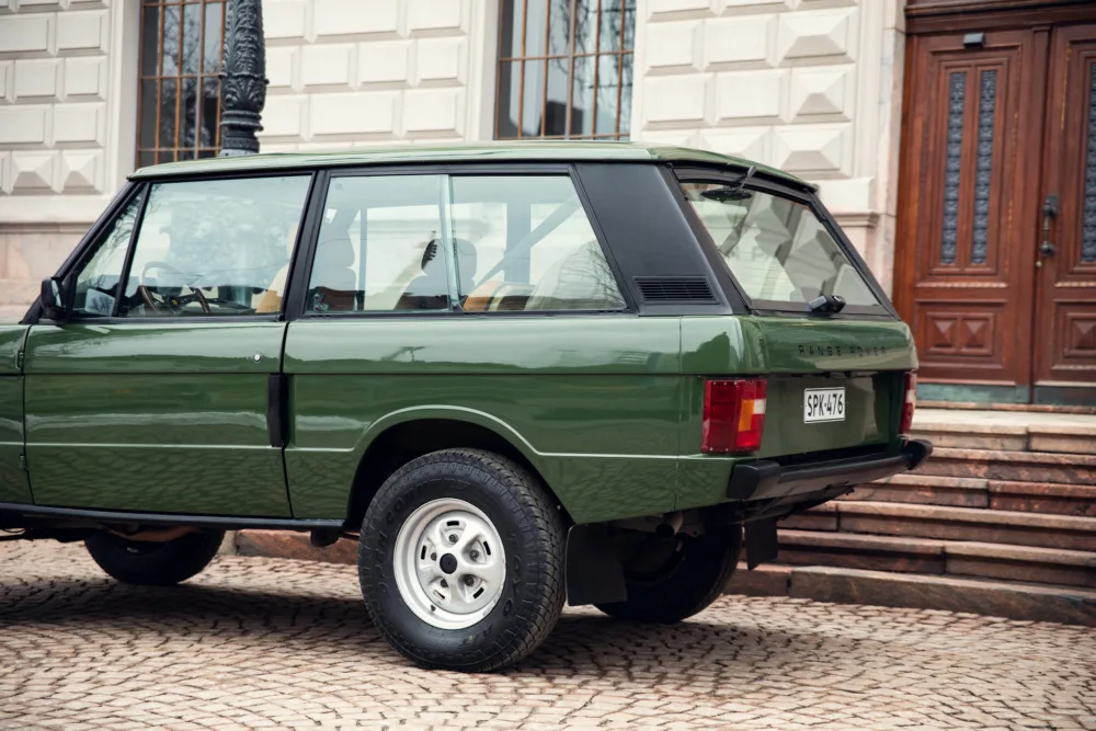 Green vintage Range Rover parked by building steps.