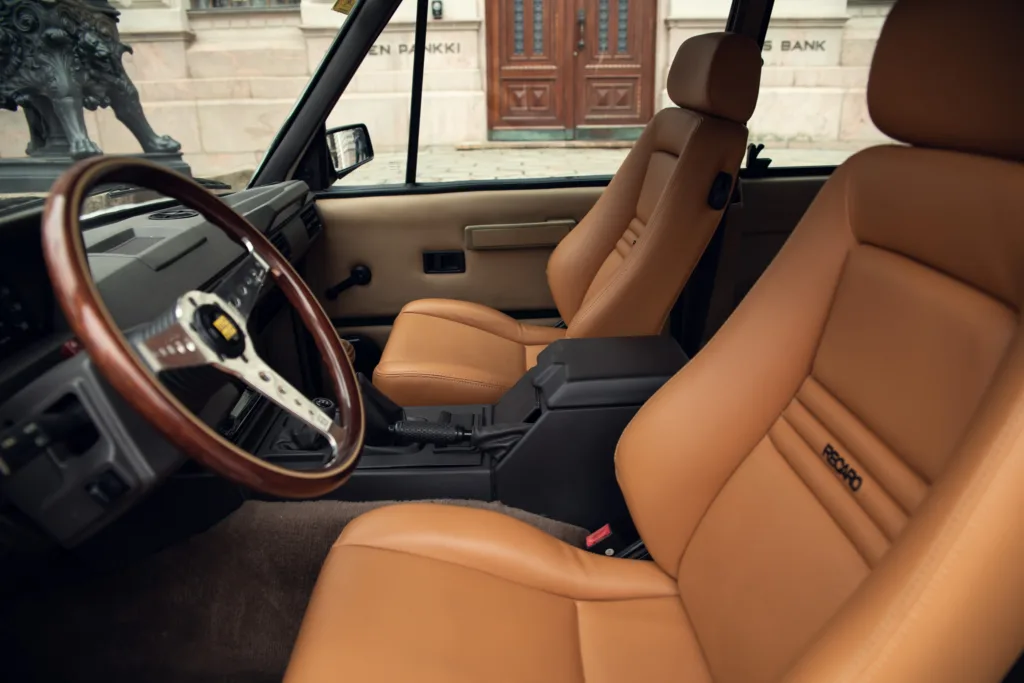 Luxury car interior with leather seats and wooden steering wheel.