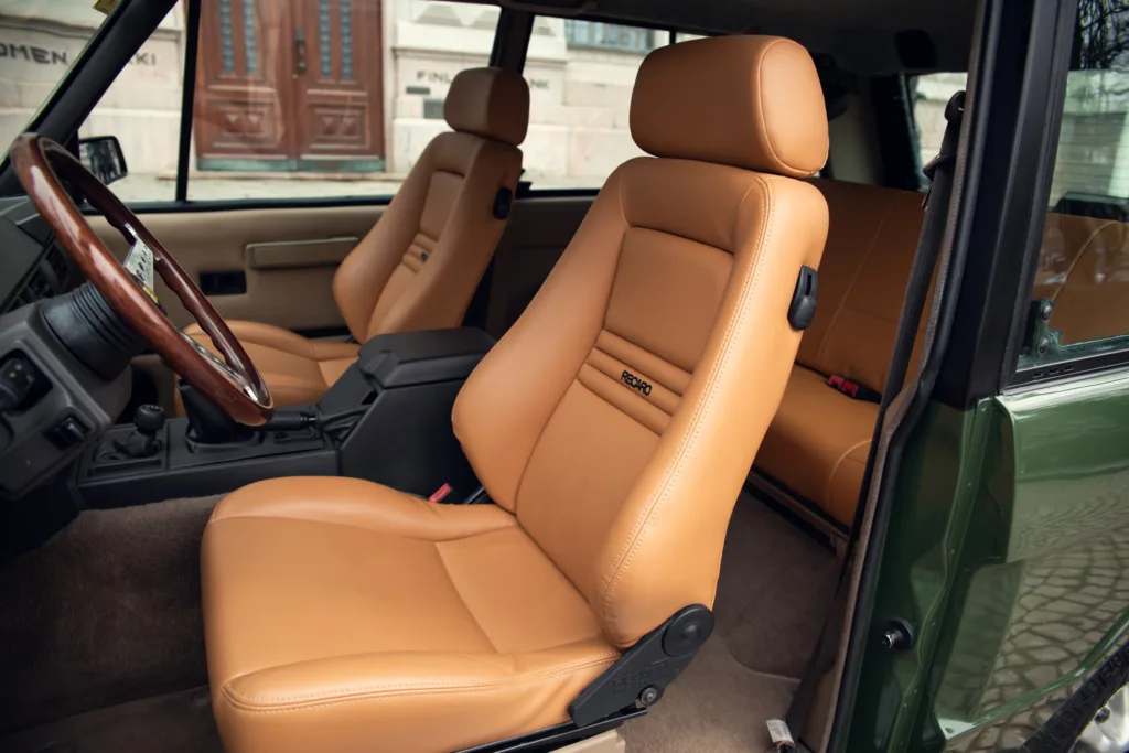 Vintage car interior with leather seats and wooden steering wheel.