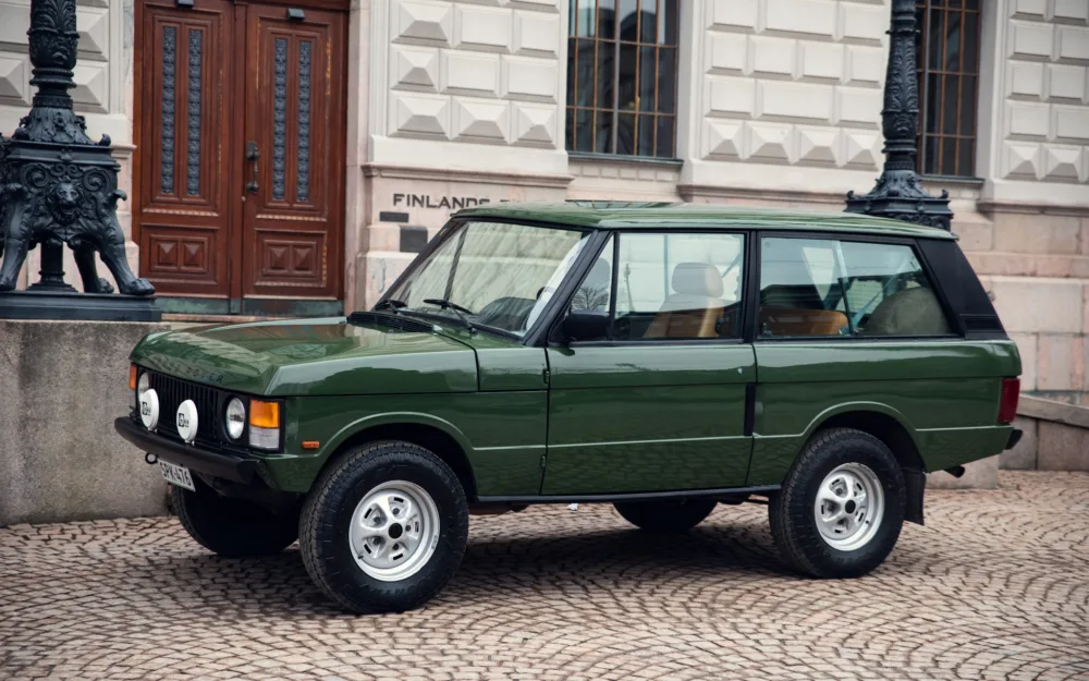 Green vintage SUV parked near historic building.