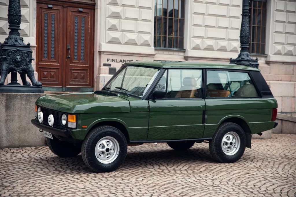 Green vintage SUV parked near historic building.