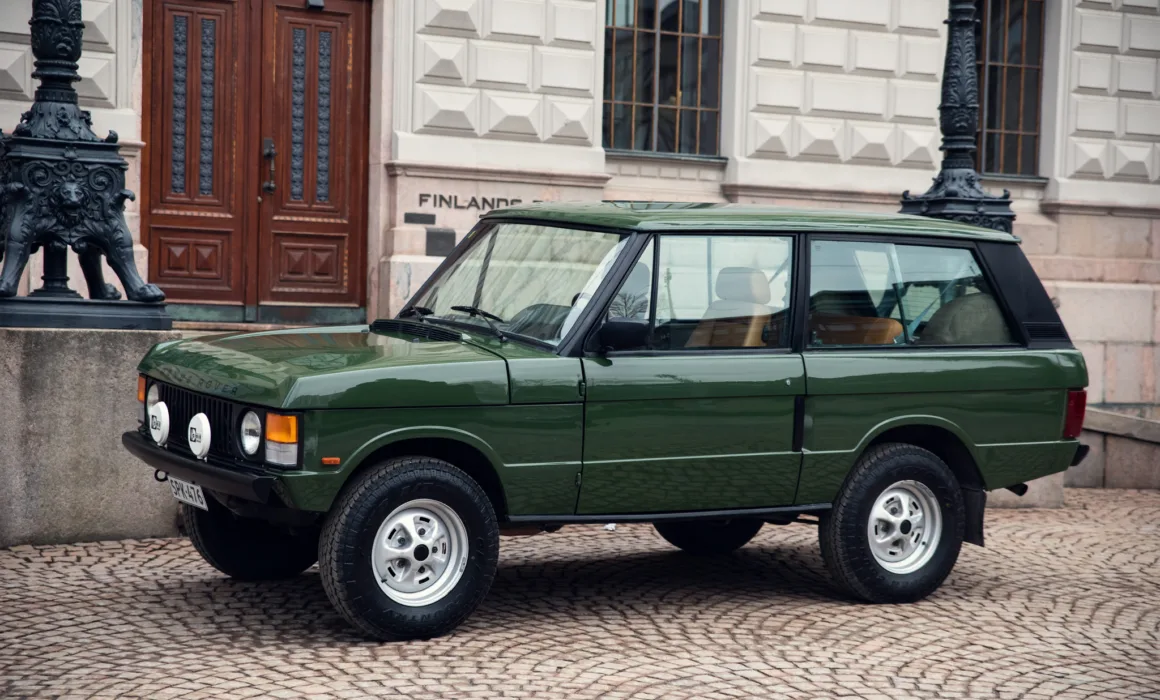 Green vintage SUV parked near historic building.