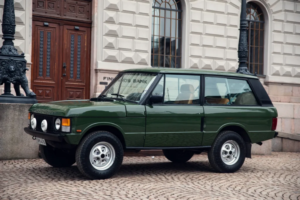 Vintage green SUV parked on cobblestone street.