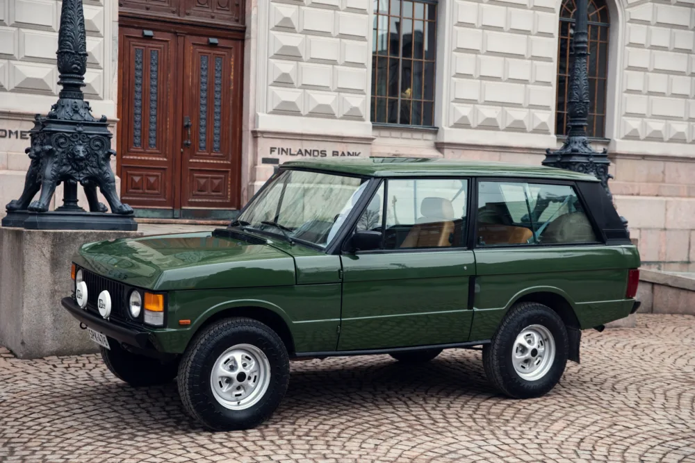 Green vintage SUV parked outside historic building.