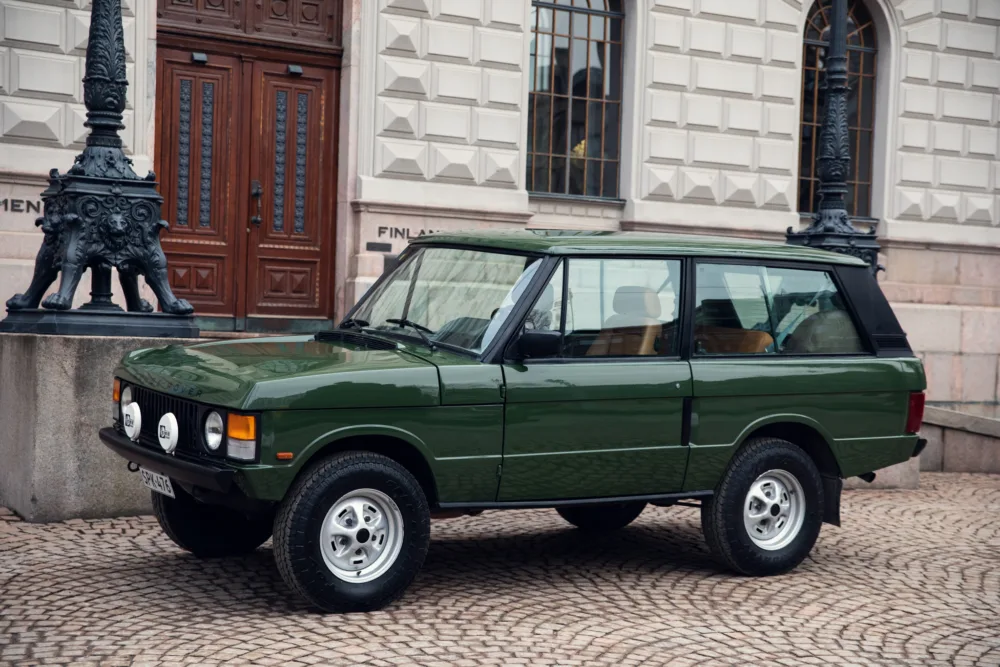 Vintage green SUV parked by historic building.