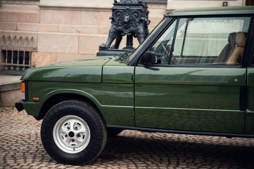 Classic green SUV parked on cobblestone street.
