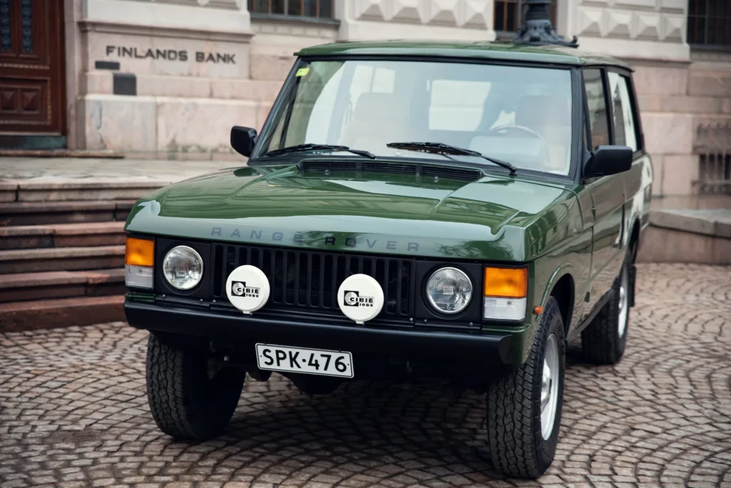 Vintage green Range Rover parked on cobblestone street.