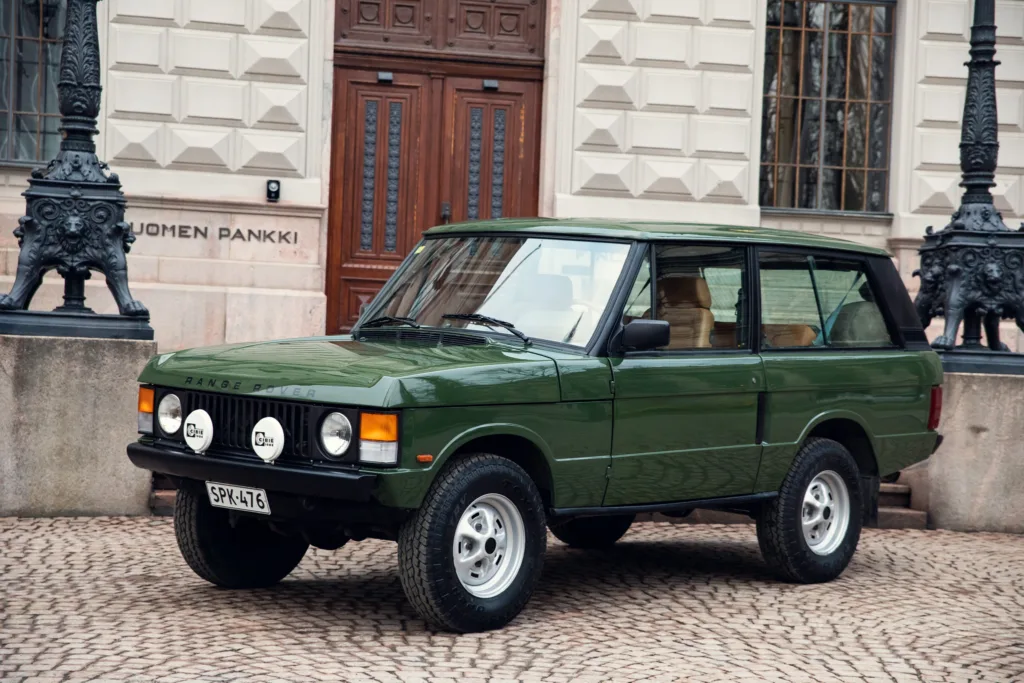 Vintage green Range Rover parked outside building.