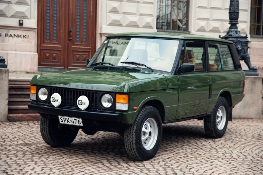 Vintage green Range Rover parked on cobblestone street.