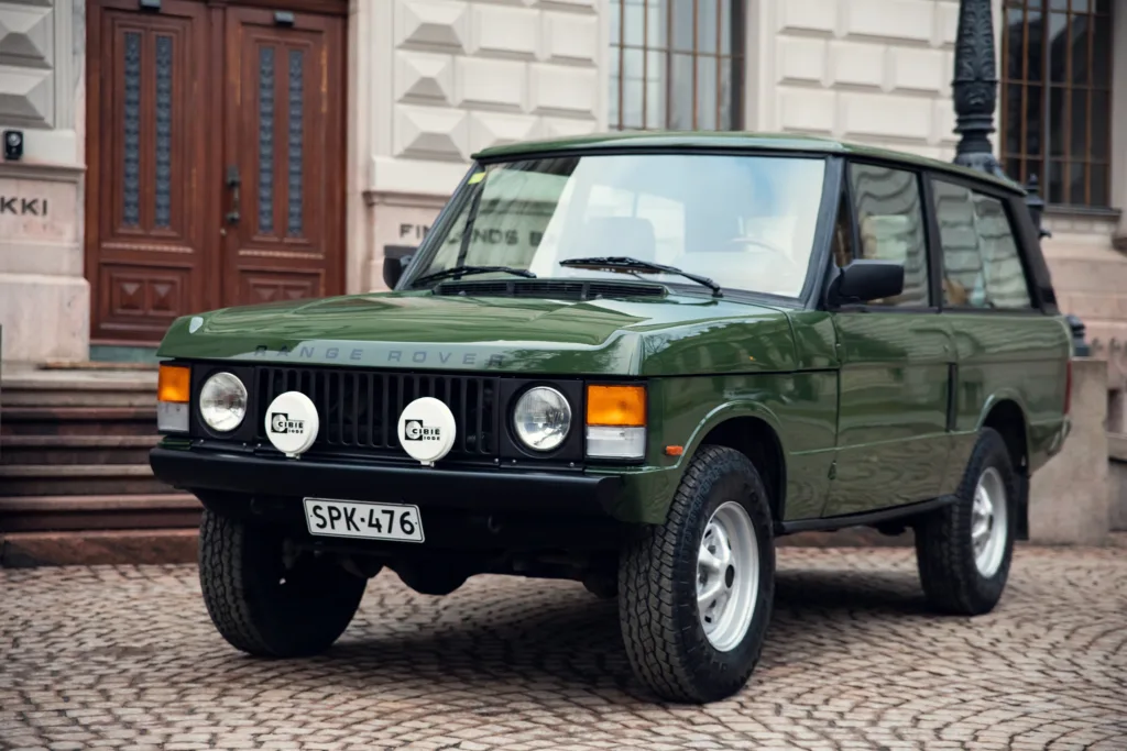 Vintage green Range Rover parked on cobblestone street.