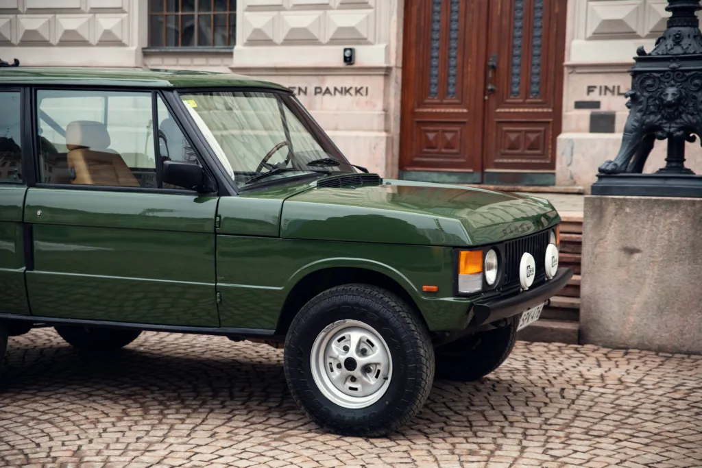 Vintage green SUV parked on cobblestone street.