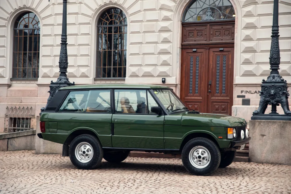 Vintage green SUV parked in historic city square.