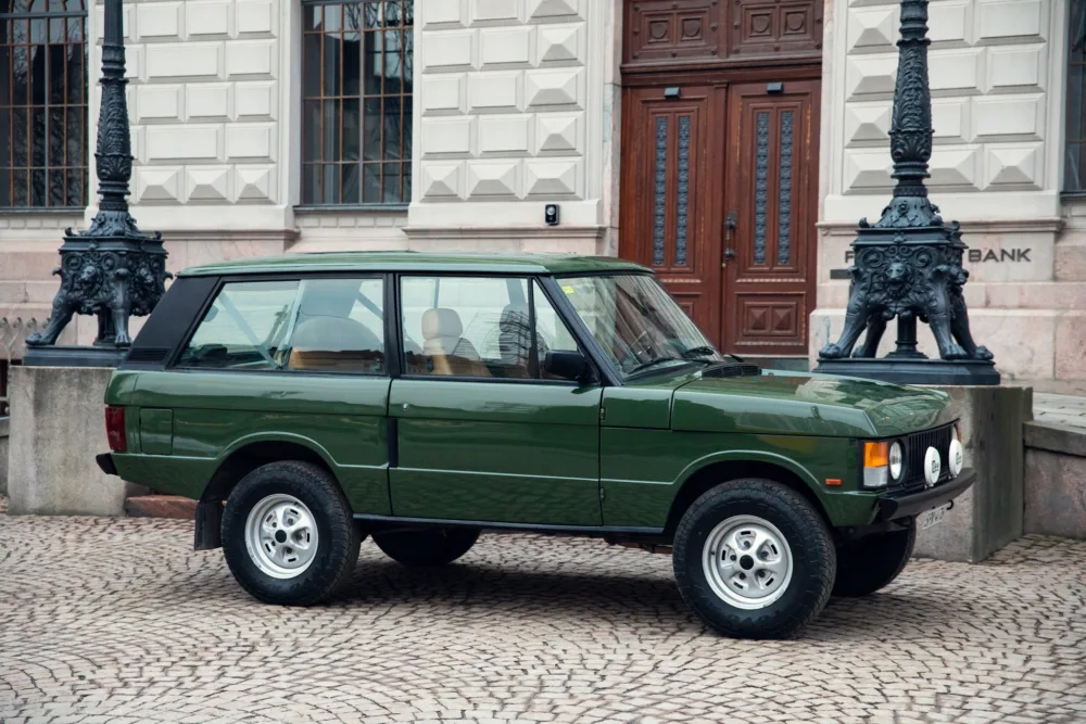 Green vintage SUV parked by historic building.