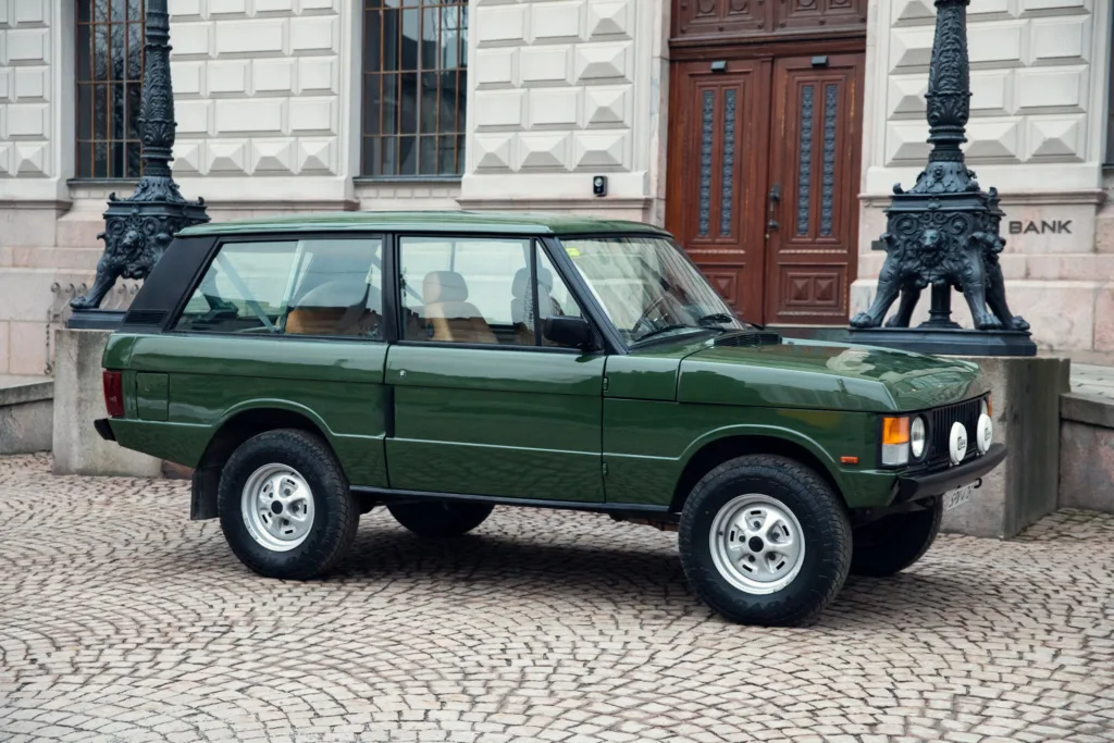 Green vintage SUV parked on cobblestone street.