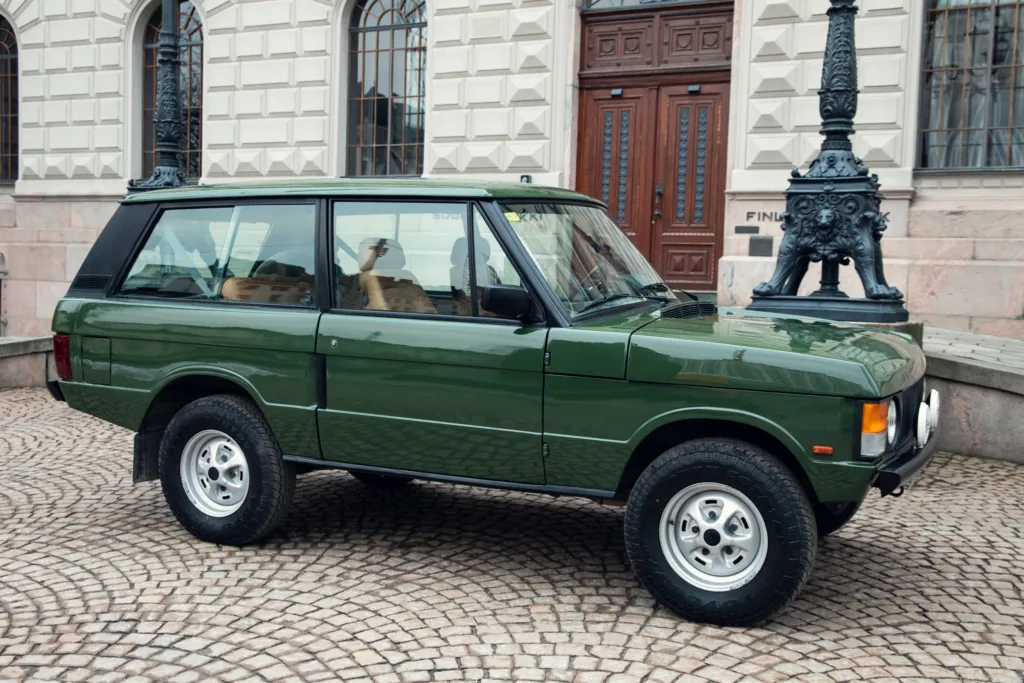 Vintage green SUV parked on cobblestone street.
