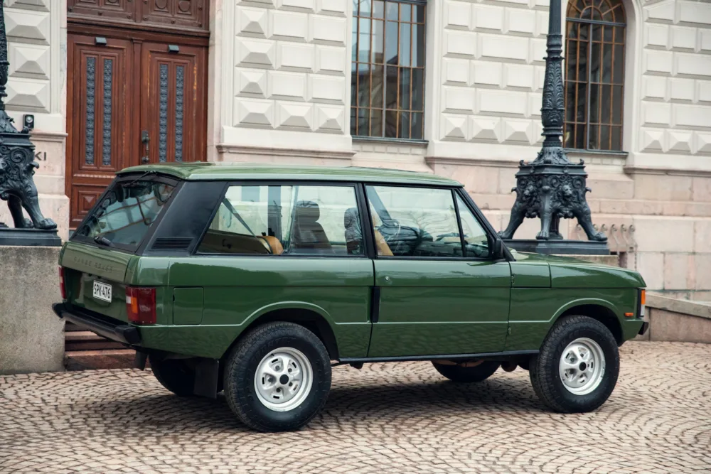 Vintage green SUV parked near historical building.