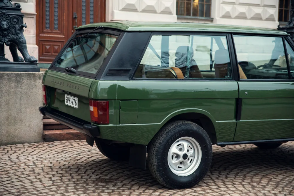 Green Range Rover parked on cobblestone street.
