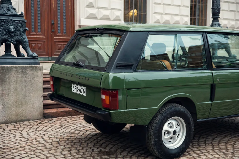 Vintage green Range Rover parked on cobblestone street.