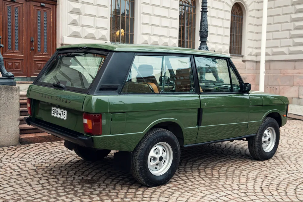 Vintage green Range Rover parked on cobblestone.