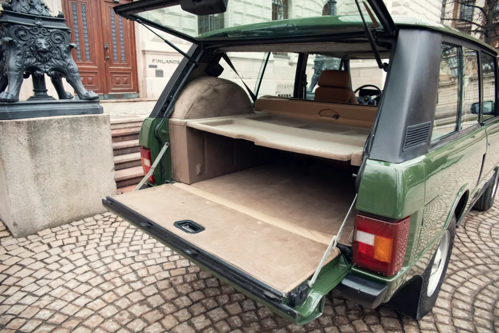 Green vintage station wagon with open trunk, city backdrop.