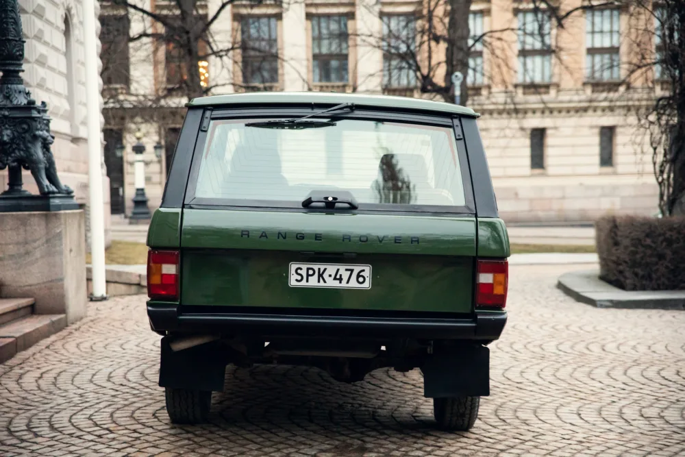 Green Range Rover parked on cobblestone street.