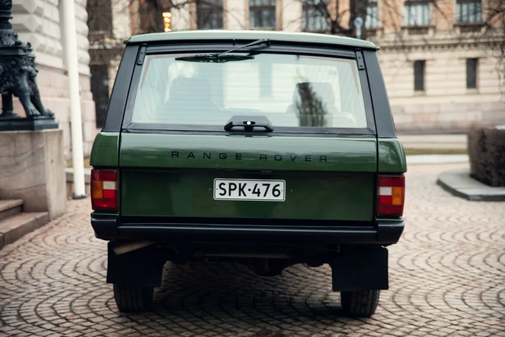Green classic Range Rover parked on cobblestone street.
