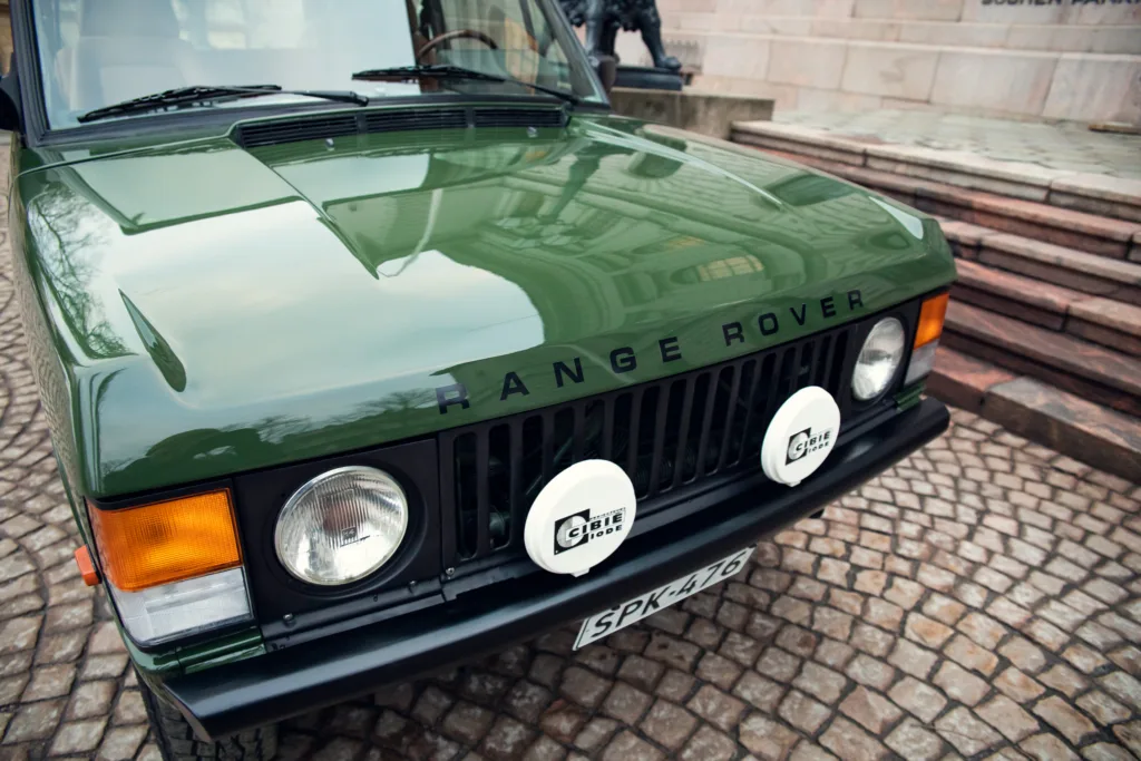 Green Range Rover classic front view on cobblestone street.