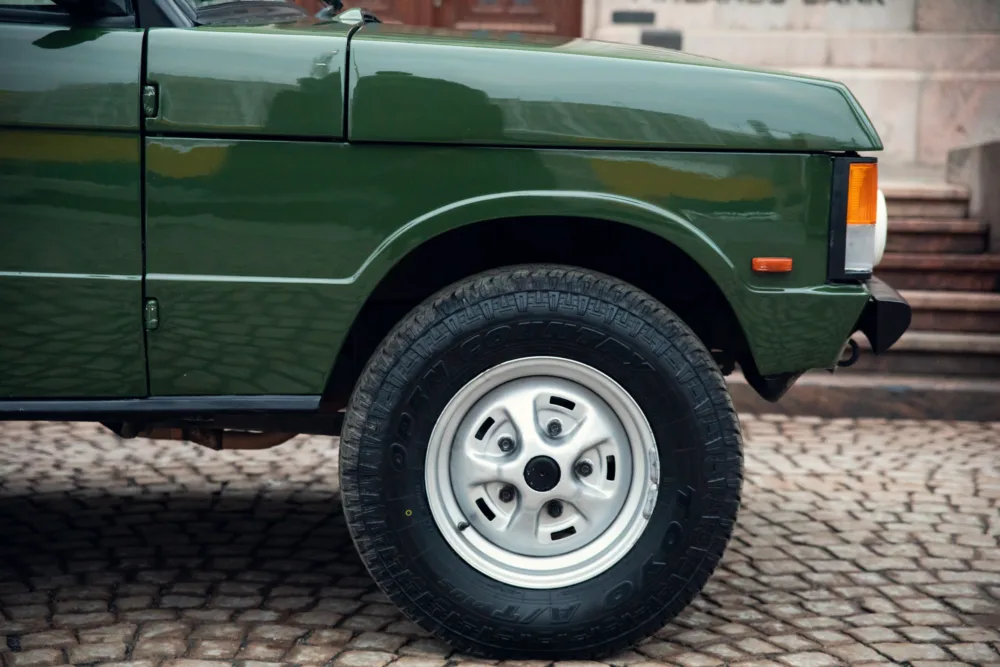 Green SUV and tire close-up on cobblestone background.