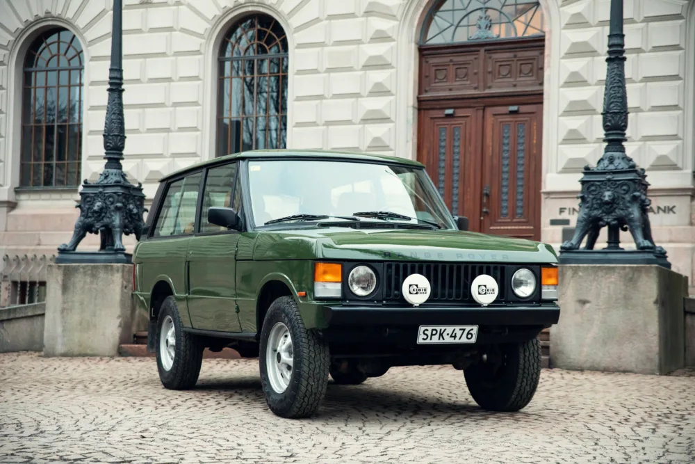 Vintage green Range Rover parked in front of building.