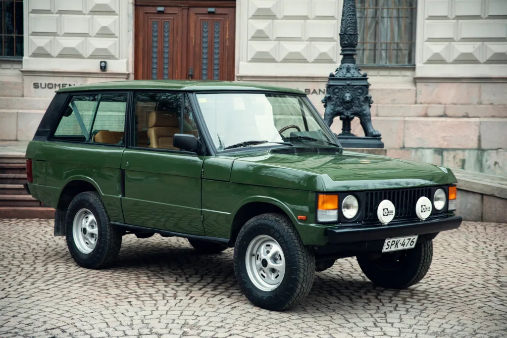 Green vintage SUV parked on cobblestone street.
