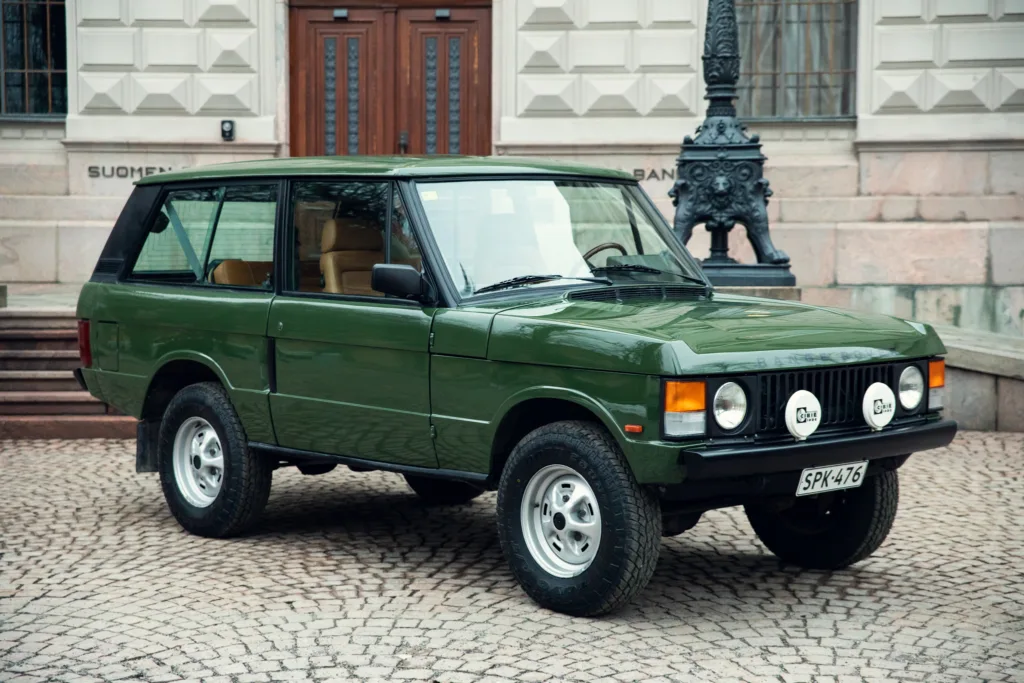 Vintage green SUV parked on cobblestone street.